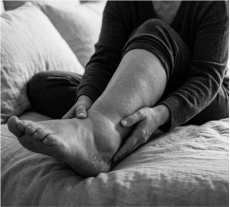 Woman gently holding her ankle while sitting on a bed